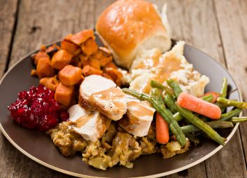 A high angle close up shot of a brown plate containing a bountiful thanksgiving turkey dinner. Shot on a grungy old wooden table