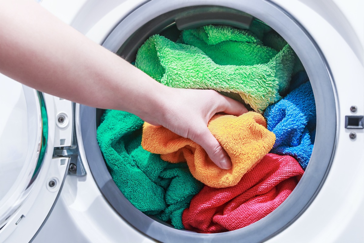 hand and puts the laundry into the washing machine