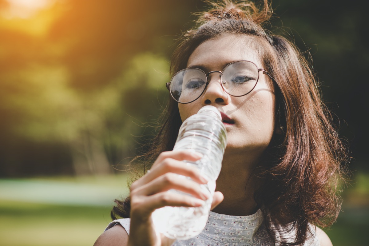 mujer bebiendo agua embotellada en el parque verde de verano