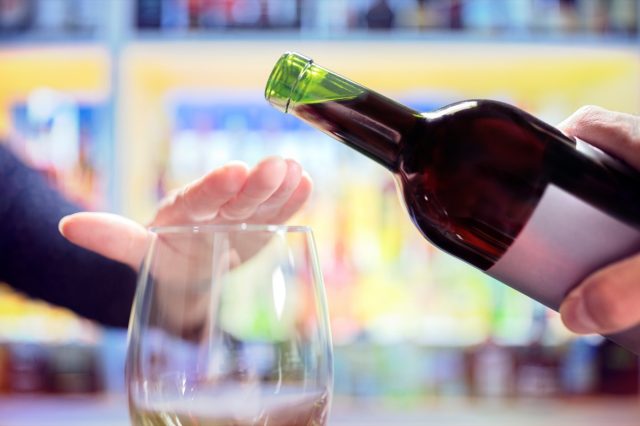 Woman refusing more alcohol from wine bottle in bar