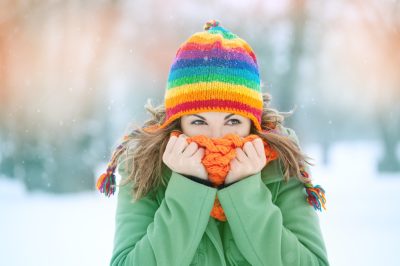 woman in snow with scarf on her face trying to warm herself