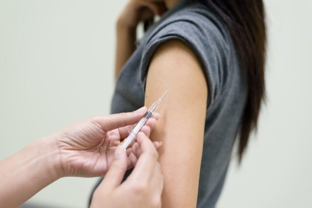 Schließen Sie die Hand des Arztes, die zur Impfung in die Schulter der Patientin spritzt