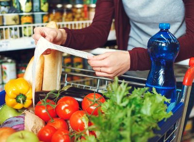 Woman looking at a receipt with full grocery cart at the grocery store