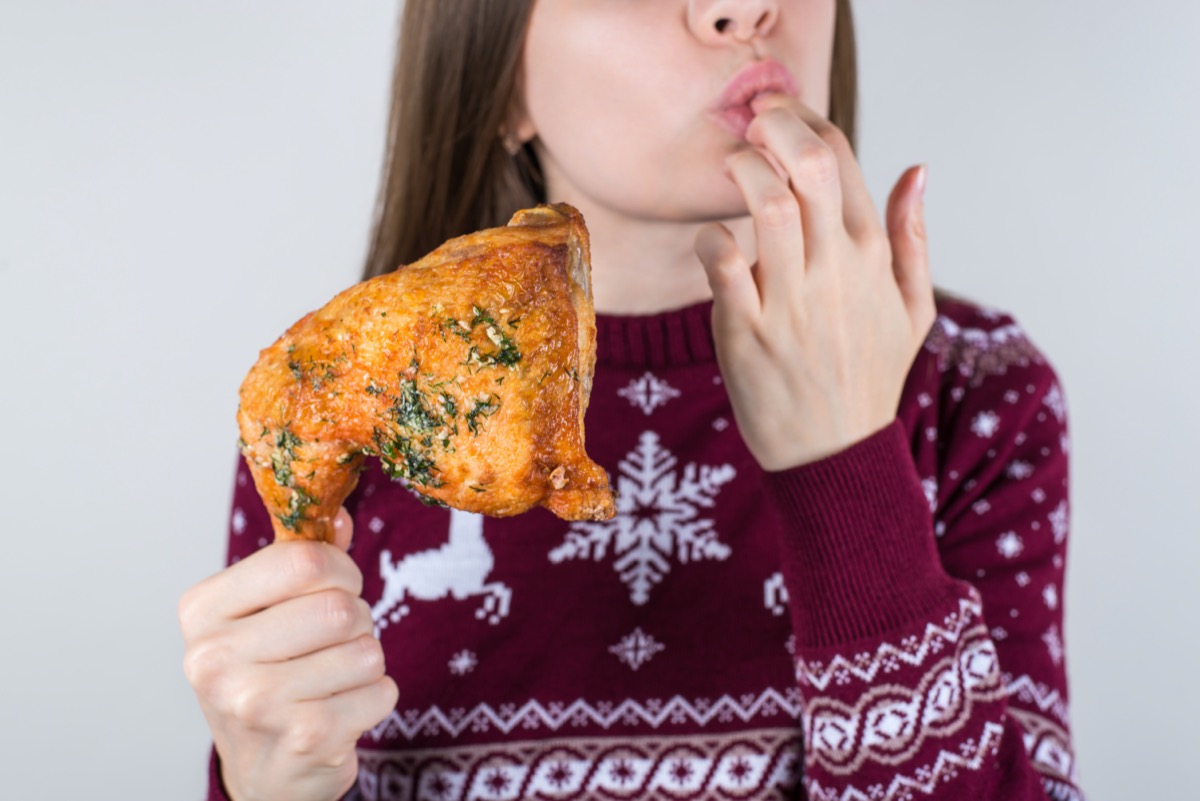 Woman wearing holiday sweater eating fired chicken and licking fingers in winter