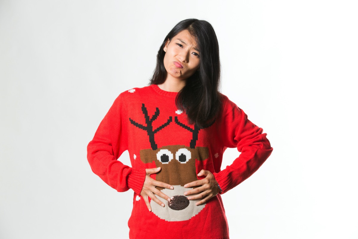 woman in Christmas sweater showing she has eaten too much food