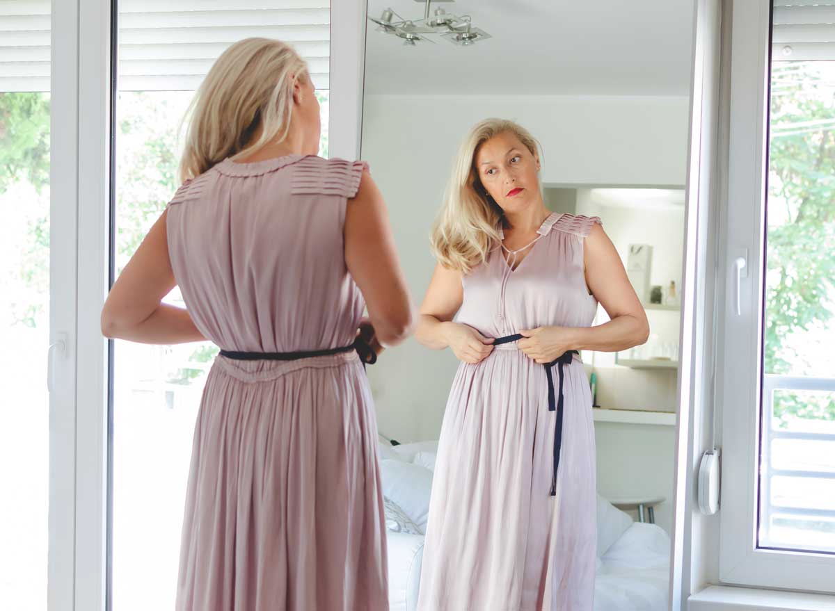Woman putting on dress looking in mirror