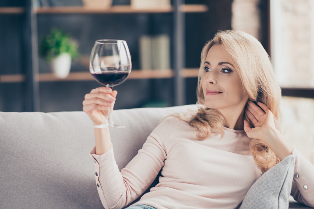 woman sitting on couch having raised glass with red wine in hand