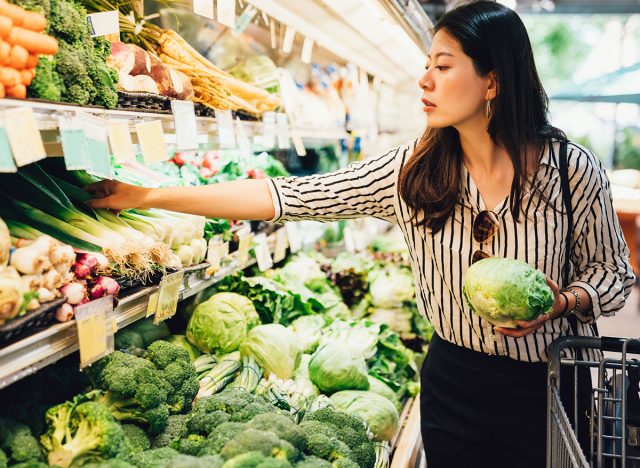 Woman holding lettuce and grabbing more produce at the grocery store