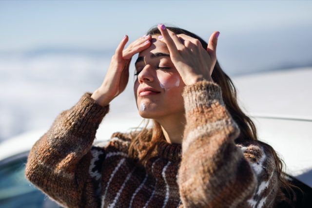 woman applying sunscreen on her face in snowy mountains in winter