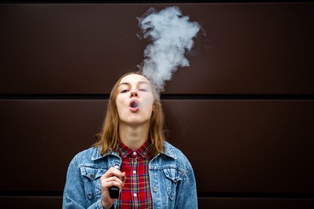 Girl in casual wear smoking an electronic cigarette