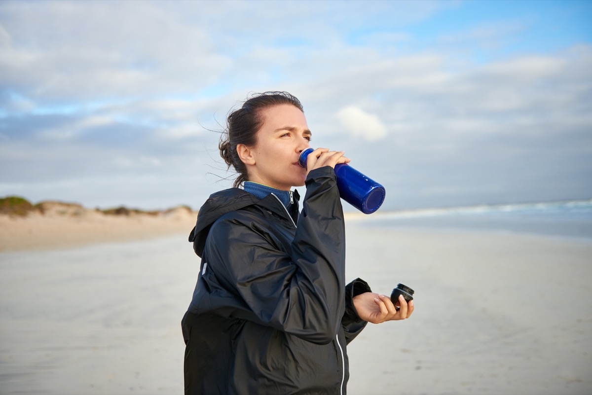 woman on a winter beach drinking from her water bottle