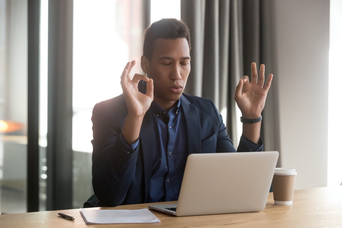 Young calm black businessman meditating during working day at office