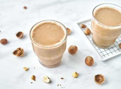 chocolate hazelnut smoothie in two glasses with hazelnuts around