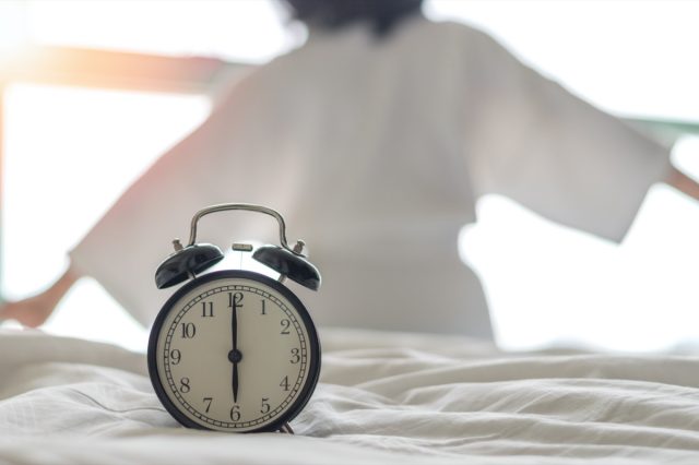 Woman on bed wake up stretching in bedroom with alarm clock at 6.00 a.m. morning.