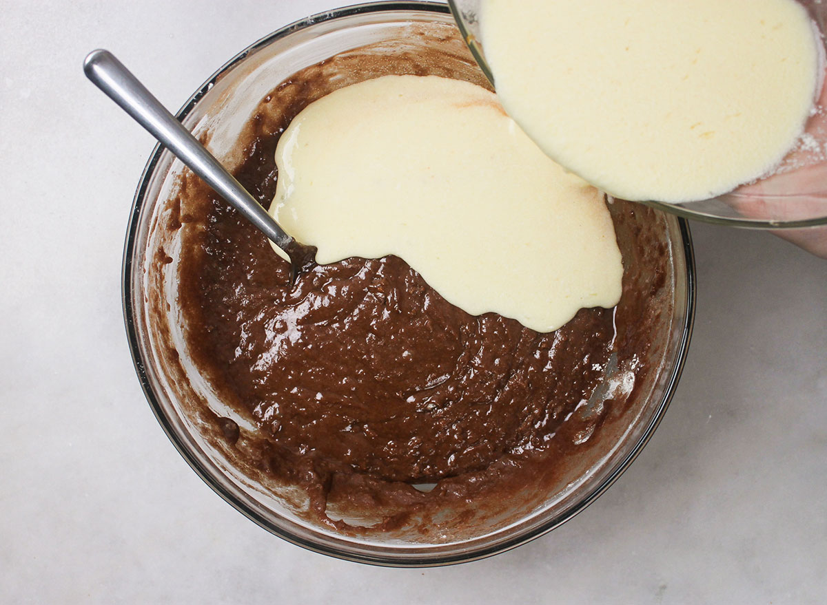 adding creamy ingredients to chocolate mixture in a bowl for coca cola cake