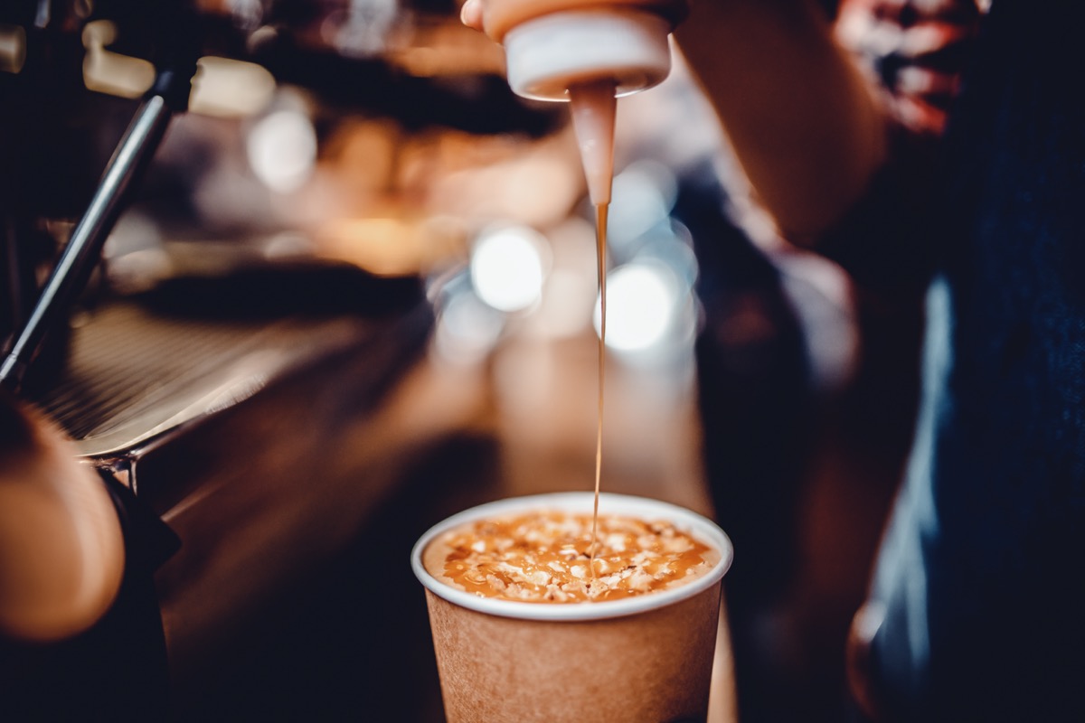 bartender before serving, pours caramel syrup, topping into finished drink in paper cup