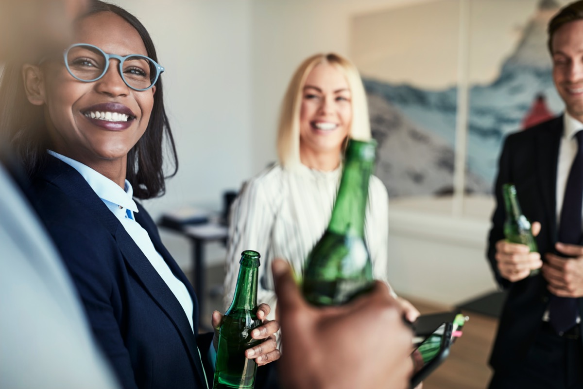 African American businesswoman talking and having drinks with a diverse group of colleagues in an office after work