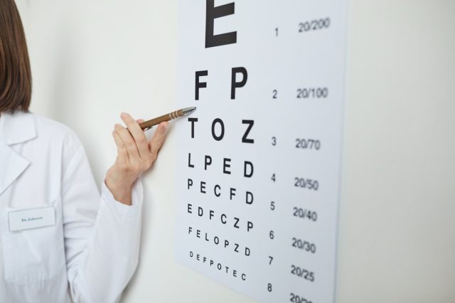 Close up of female hand pointing at eye chart with Latin letters during eyesight test in ophthalmology clinic