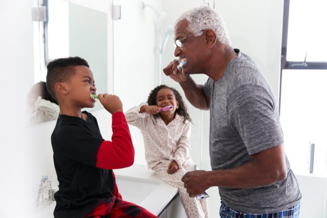 Grandfather In Bathroom Wearing Pajamas Brushing Teeth With Grandchildren