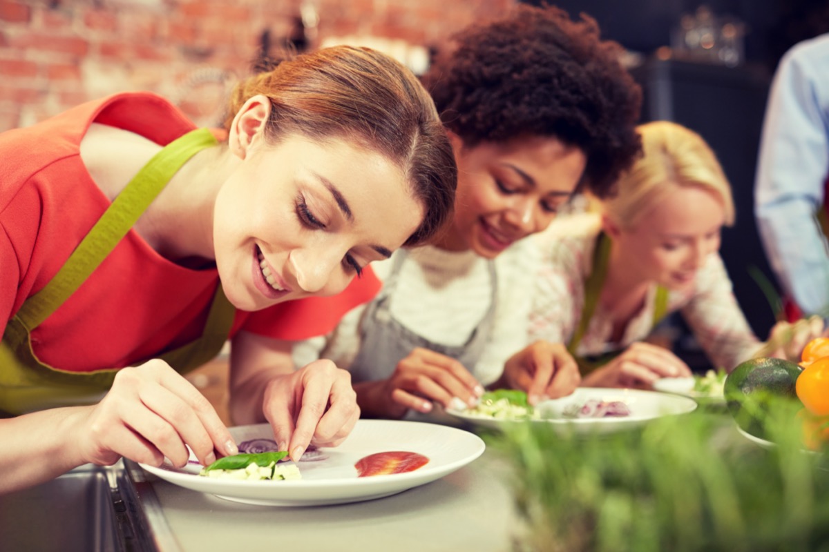 happy women cooking and decorating plates with dishes in kitchen