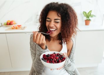 Young healthy laughing african woman eating breakfast and fruits in kitchen in the morning