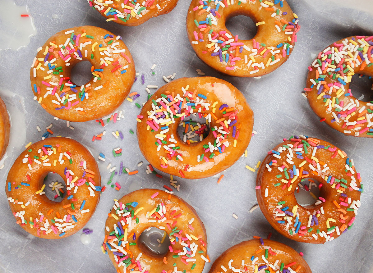 adding sprinkles to hot donuts with glaze