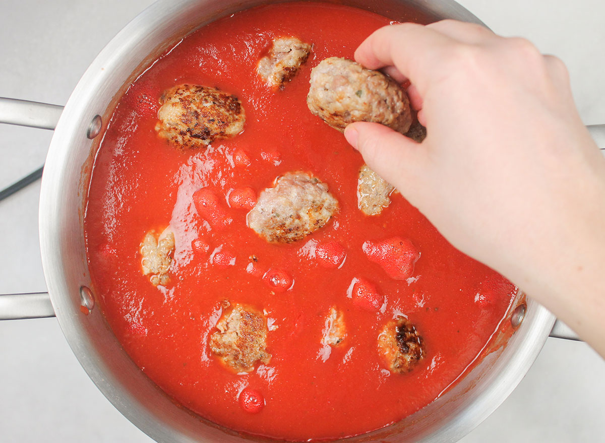 adding meatballs to tomato sauce