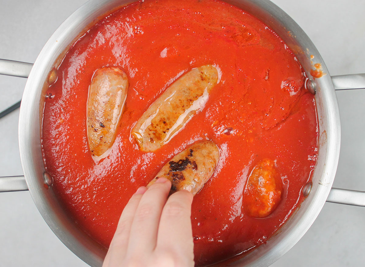 adding hot Italian sausage to pot of meatballs