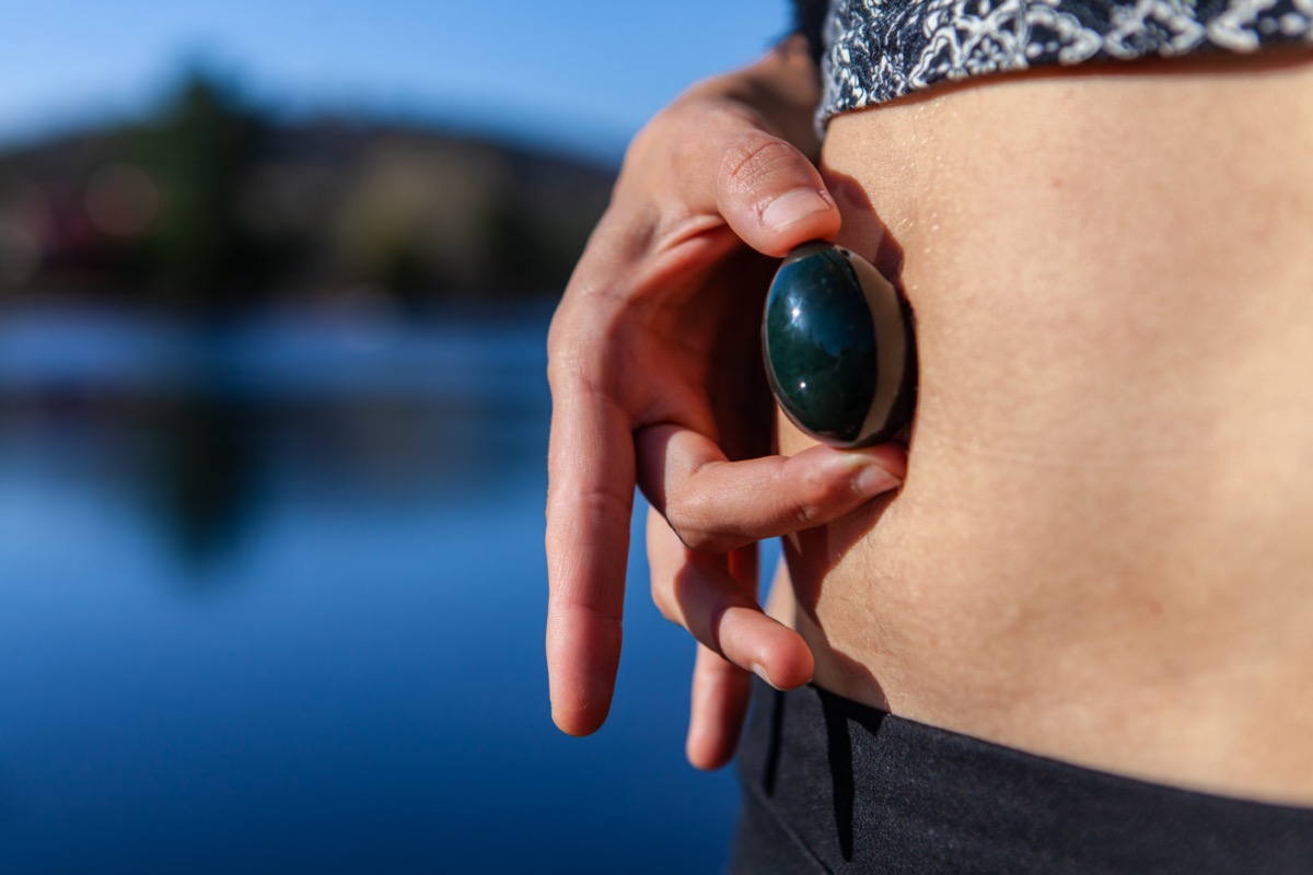 woman holding her sacred yoni jade egg to her belly button as an empowerment symbol