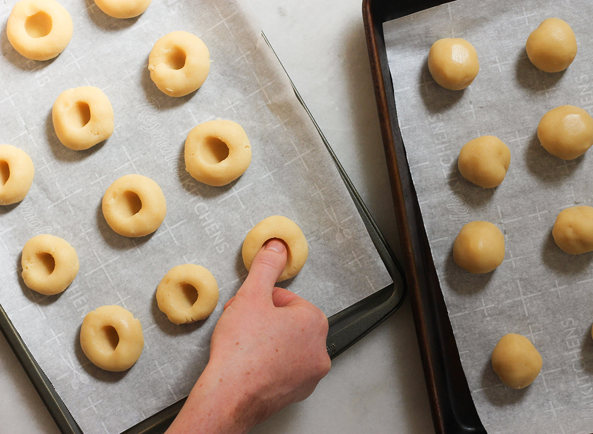 pressing thumb into thumbprint cookies on a baking sheet