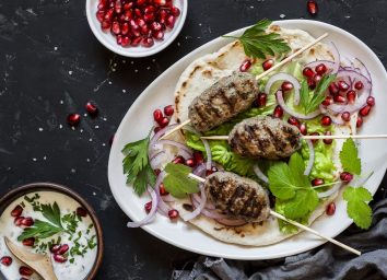 lamb kebabs on a plate with pomegranate seeds and fresh veggies