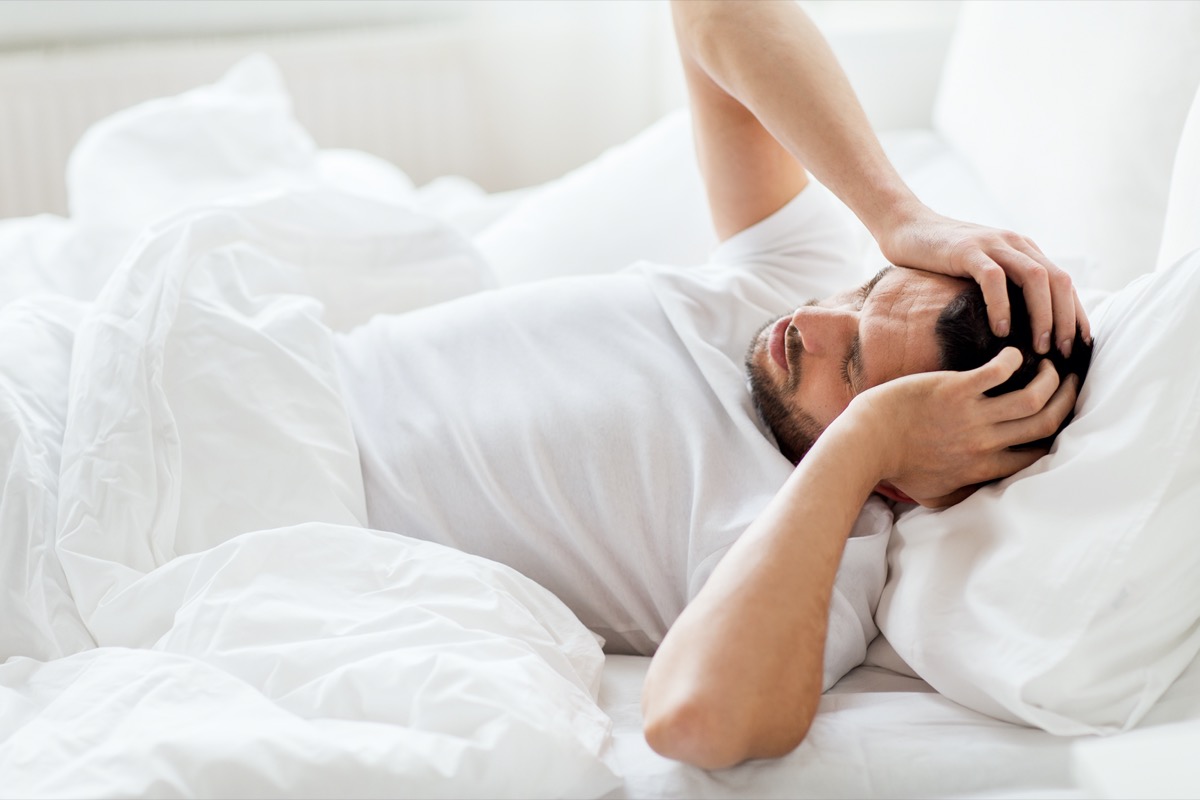 man lying in bed at home suffering from headache or hangover