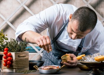 Chef sprinkling spices on dish in kitchen
