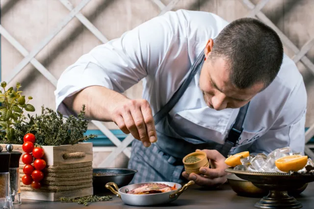 Chef sprinkling spices on dish in kitchen