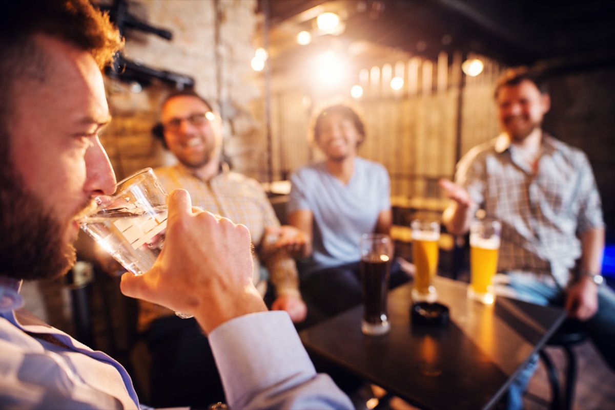 man drinking a glass of water in the local pub while his friends laughing with a beer in front