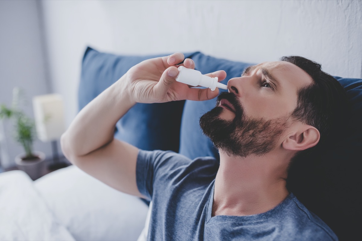 portrait of man sitting in the bed spraying drops in his nose