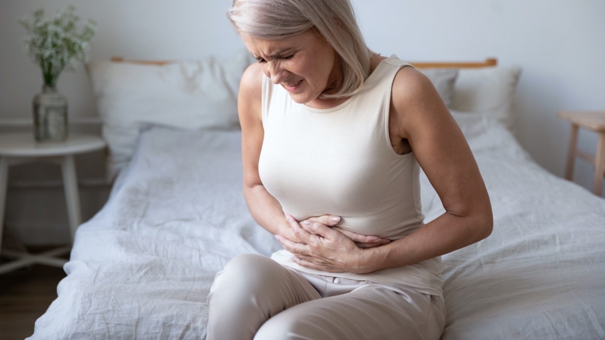 Unhealthy mature woman holding stomach and feeling uncomfortable