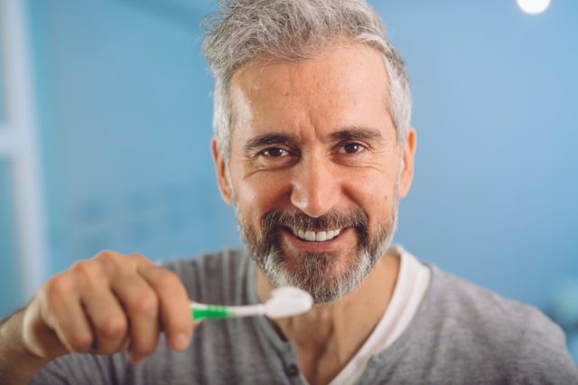 middle aged bearded gray haired man brushing his teeth