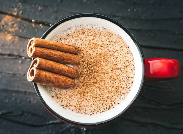 Mug of coffee and ground cinnamon sprinkled on top with two cinnamon sticks