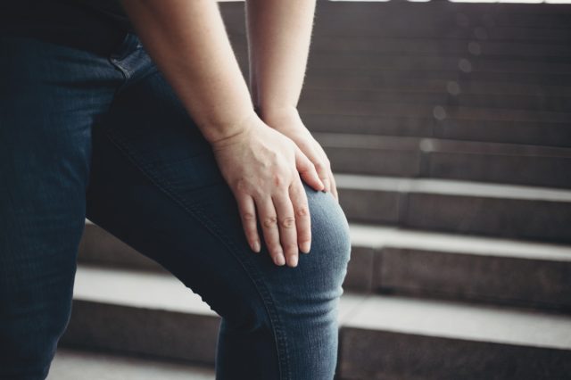 Overweight woman suffering from knee pain stepping on stairs