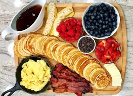 pancake board with berries chocolate chips syrup eggs bacon