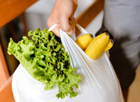man holding plastic grocery bag with lettuce and bananas