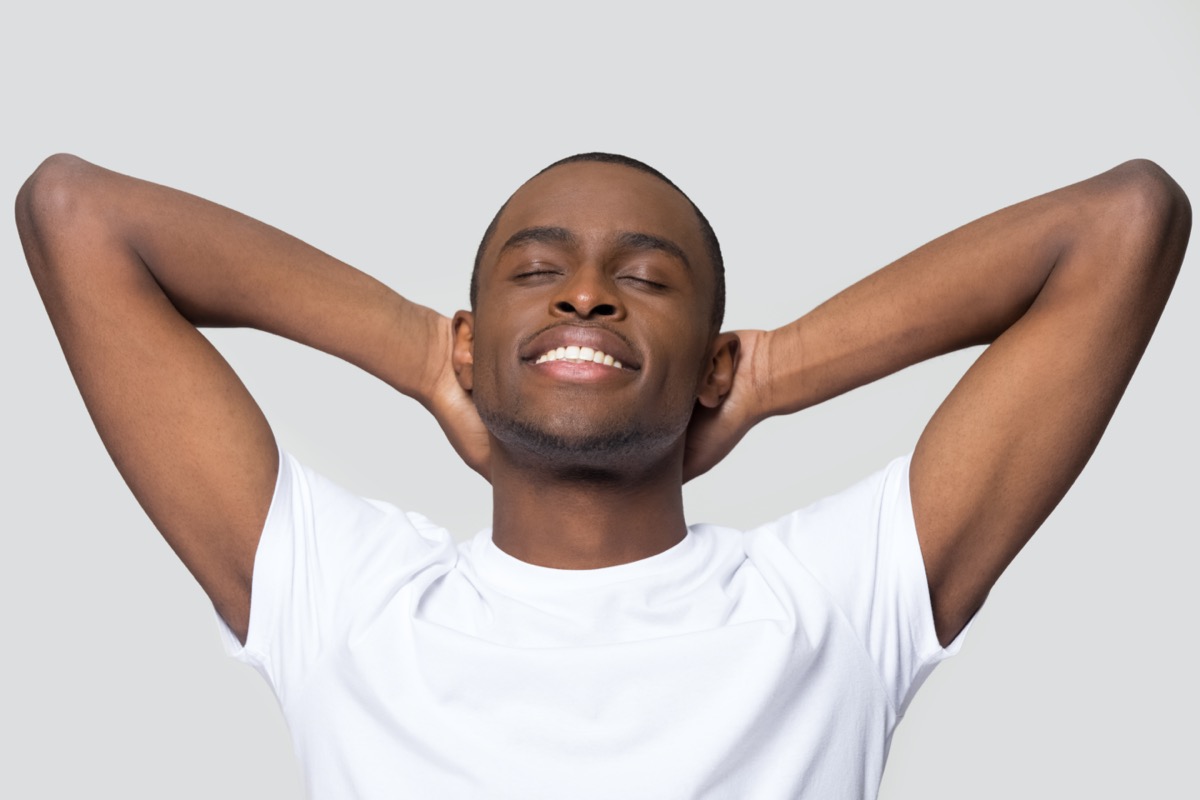 man relaxing with hands behind head, satisfied peaceful young male with closed eyes resting, enjoying free time, meditating, stretching