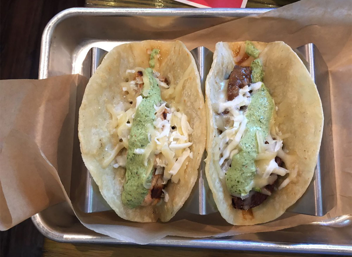two tacos with green sauce in serving tray