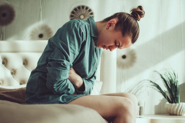 Wanita muda kesal stres menderita sakit perut dan perut saat menstruasi, PMS di kamar di rumah.  Peradangan dan infeksi.  keracunan makanan