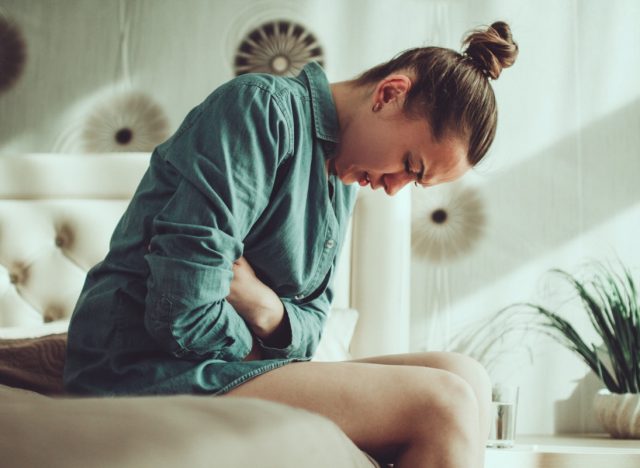 Young upset stressed woman suffering from abdominal and stomach pain during menstruation, PMS in room at home. Inflammation and infection. Food poisoning