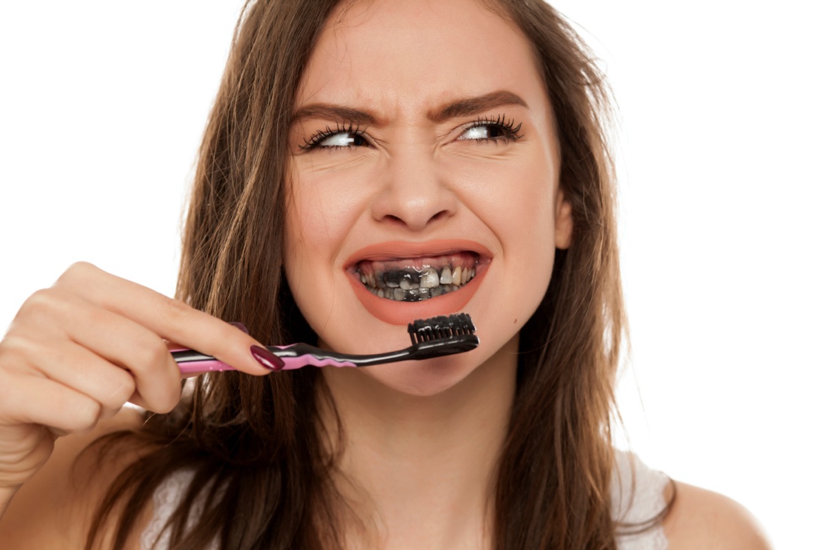 young woman brushing her teeth with a black tooth paste with active charcoal, and black tooth brush