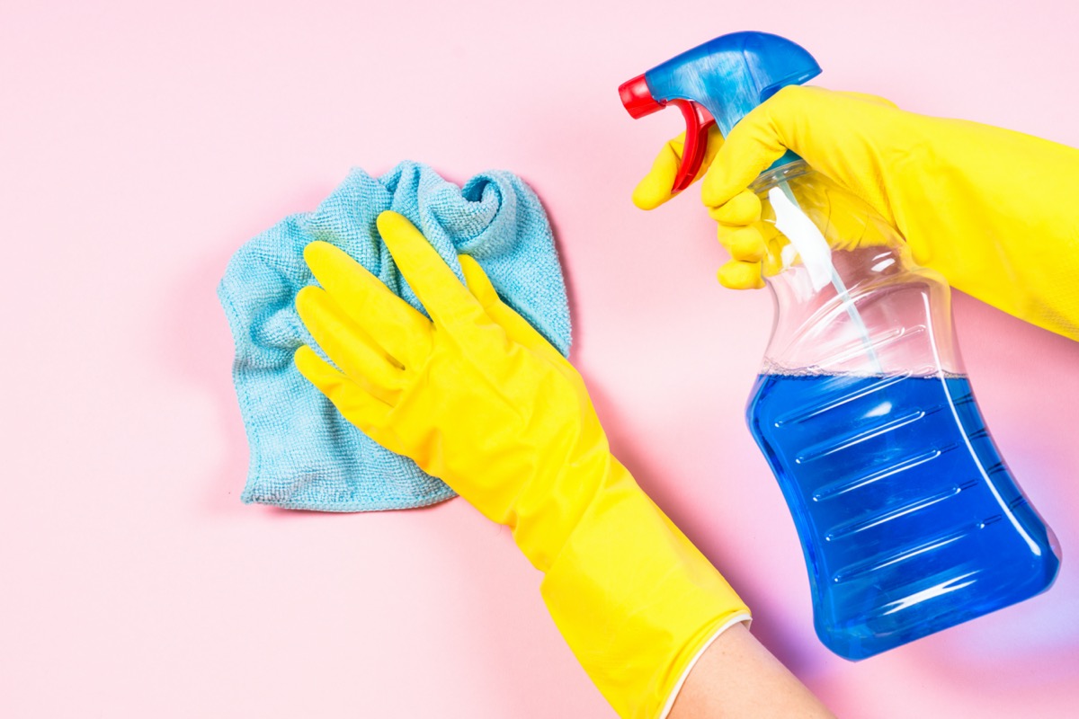 Woman cleaning pink surface indoor with microfiber rag and cleaning spray agent
