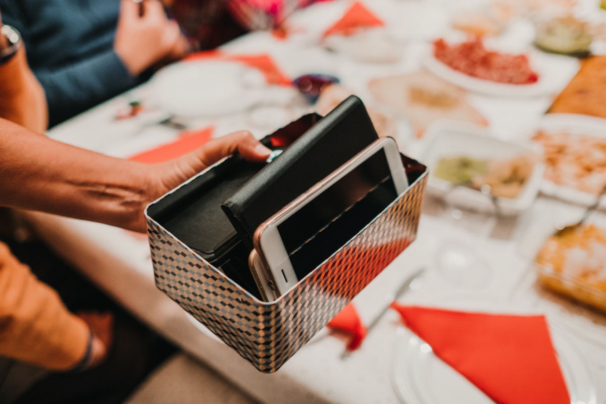 Hand of a woman holding a box full of smartphones of the guests at her dinner. They take a break with technology to have an endearing conversation. Lifestyle.