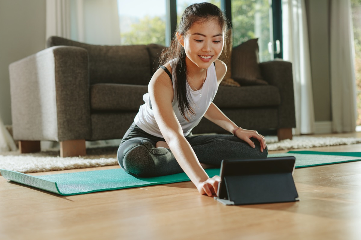 Smiling woman sitting exercise mat and watching training videos on digital tablet